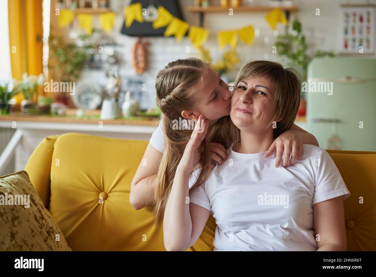 La fille embrasse maman assise sur le canapé dans la cuisine. Banque D'Images