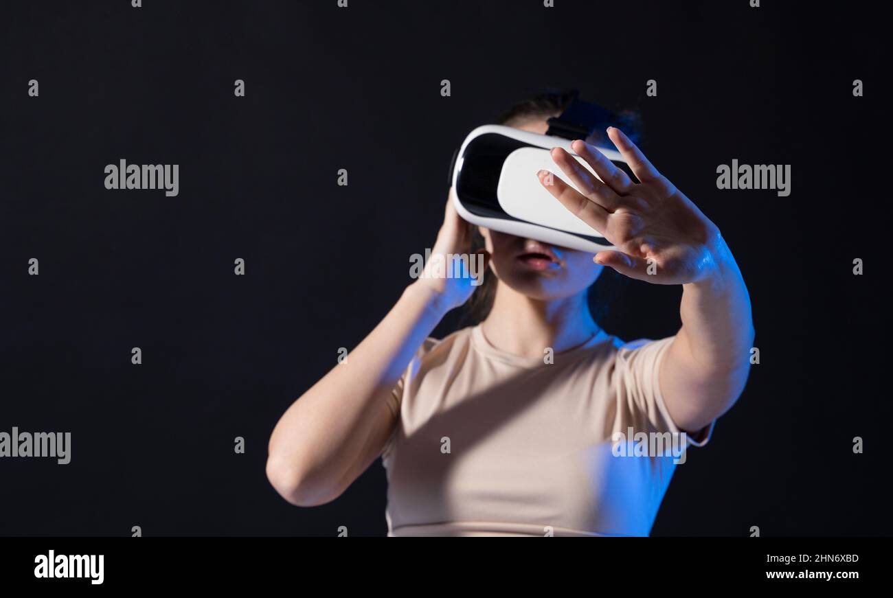 Gros plan d'une jeune femme se tient en studio, portant des lunettes VR avec une main dans l'air et essayant de toucher un peu dans l'espace virtuel. Réalité virtuelle Banque D'Images