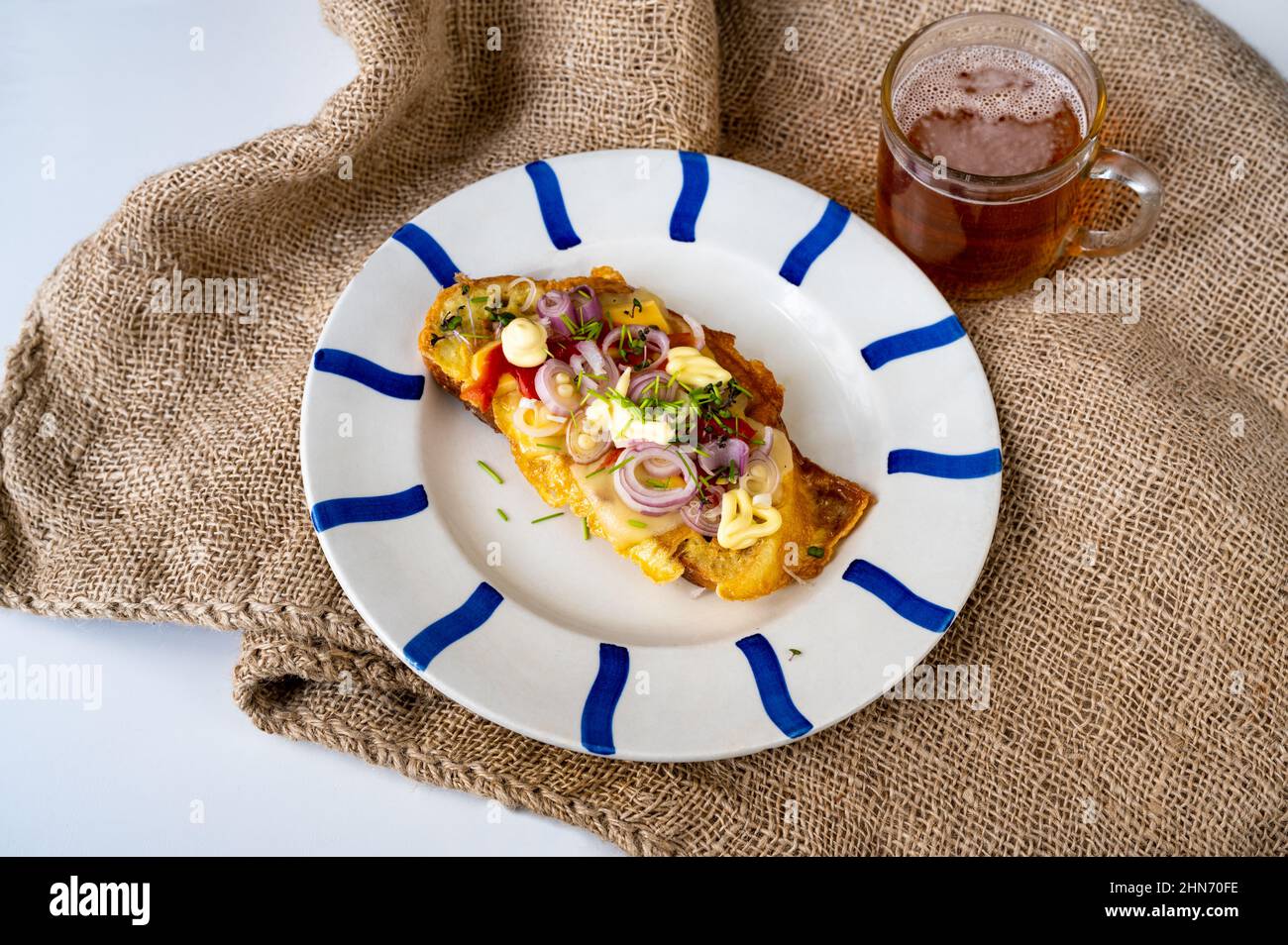 Pain garni d'œufs frits, oignon, fromage, poivron rouge, pousse-ciboulette et mayonnaise, verre de thé sur jute. Petit déjeuner fermier simple et copieux. Banque D'Images