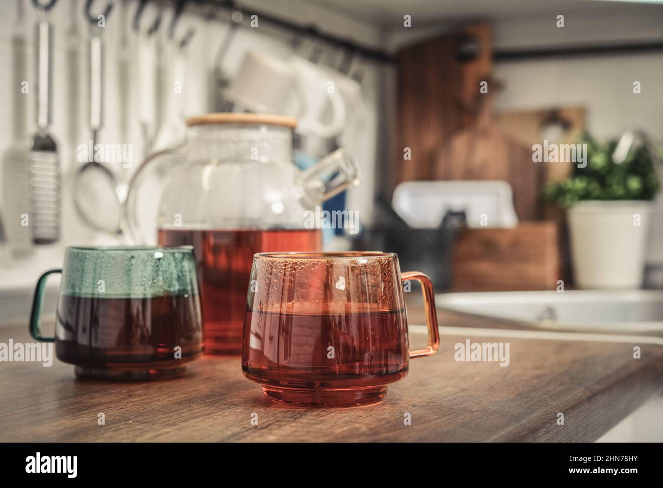 Théière en verre pleine de thé noir avec deux tasses de thé sur le plan de travail de la cuisine Banque D'Images
