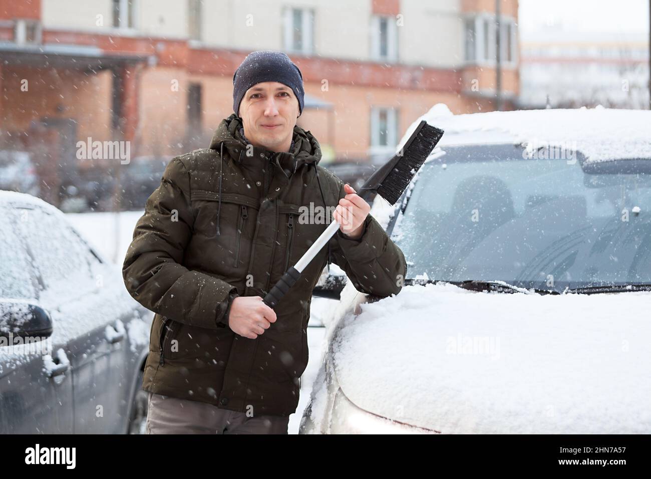 Portrait d'un homme adulte du Caucase avec un pinceau à neige dans les mains, debout près de sa voiture enneigée en hiver, une personne Banque D'Images