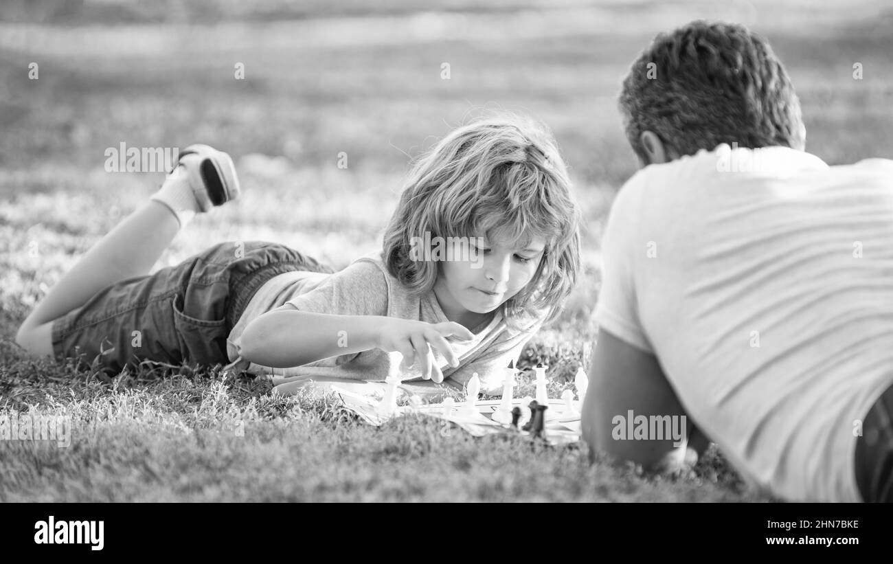 bonne famille de père et fils enfant jouant aux échecs sur l'herbe verte dans le parc extérieur, tactique Banque D'Images