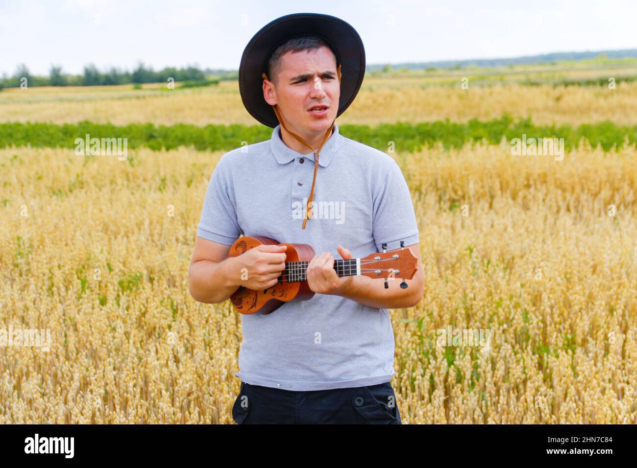 Guitare Hawaï. Jeune beau caucasien homme jouant ukulele dehors. Beau hipster Guy joue ukulele guitare sur fond de nature. Homme dans un cow-boy Banque D'Images