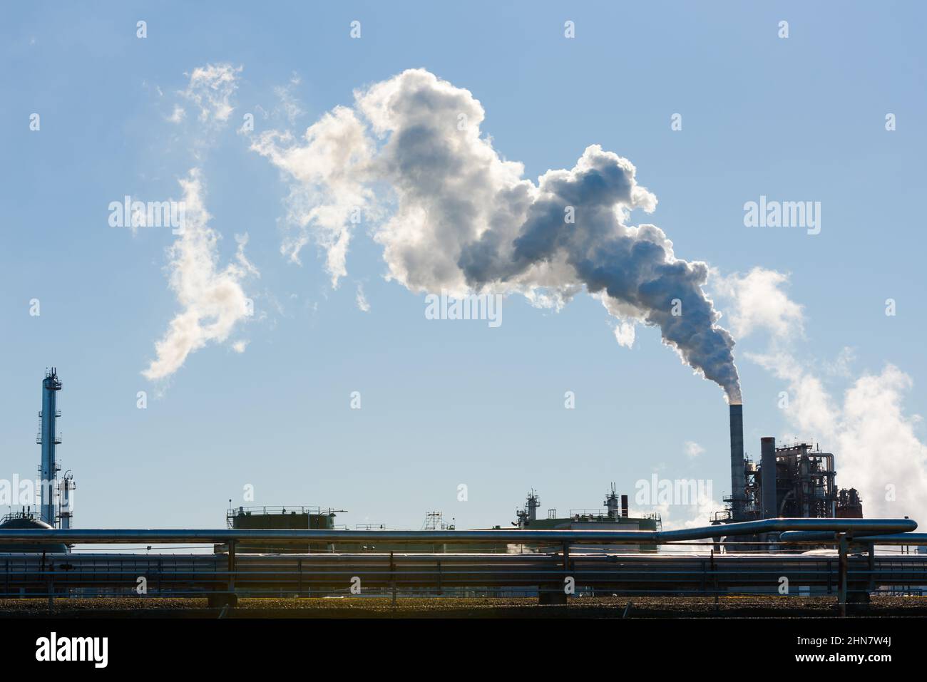 La vapeur s'écoule de la cheminée d'une usine de raffinage du pétrole contre un ciel bleu clair pendant que le panache dévie Banque D'Images