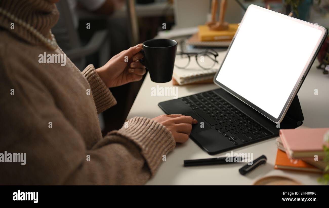 Femme indépendante, écrivain freelance sirotant un café chaud tout en travaillant sur sa tablette portable dans son bureau à domicile. Concept de travail à distance Banque D'Images