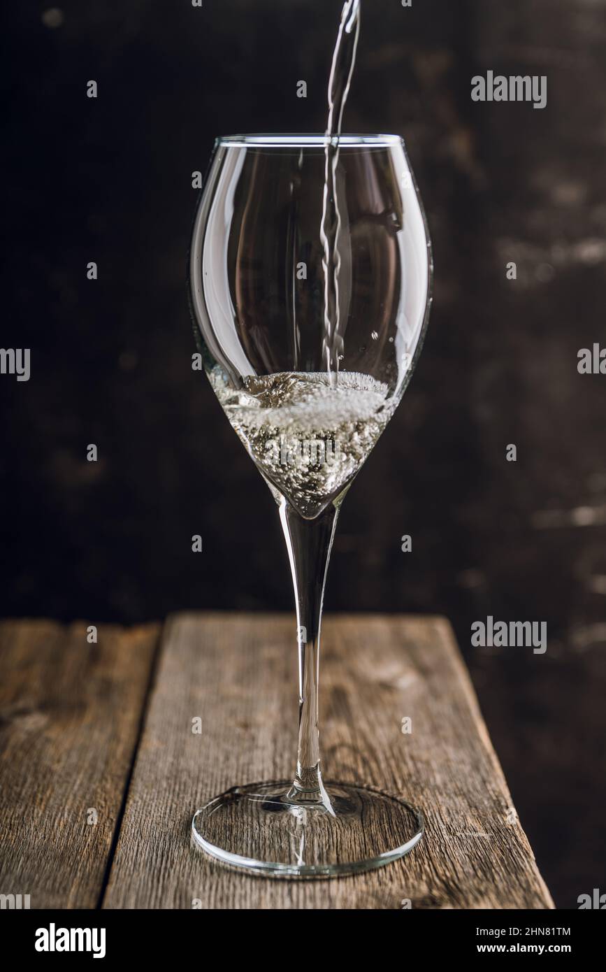 Verser le vin blanc dans le verre sur le fond rustique en bois. Mise au point sélective. Banque D'Images