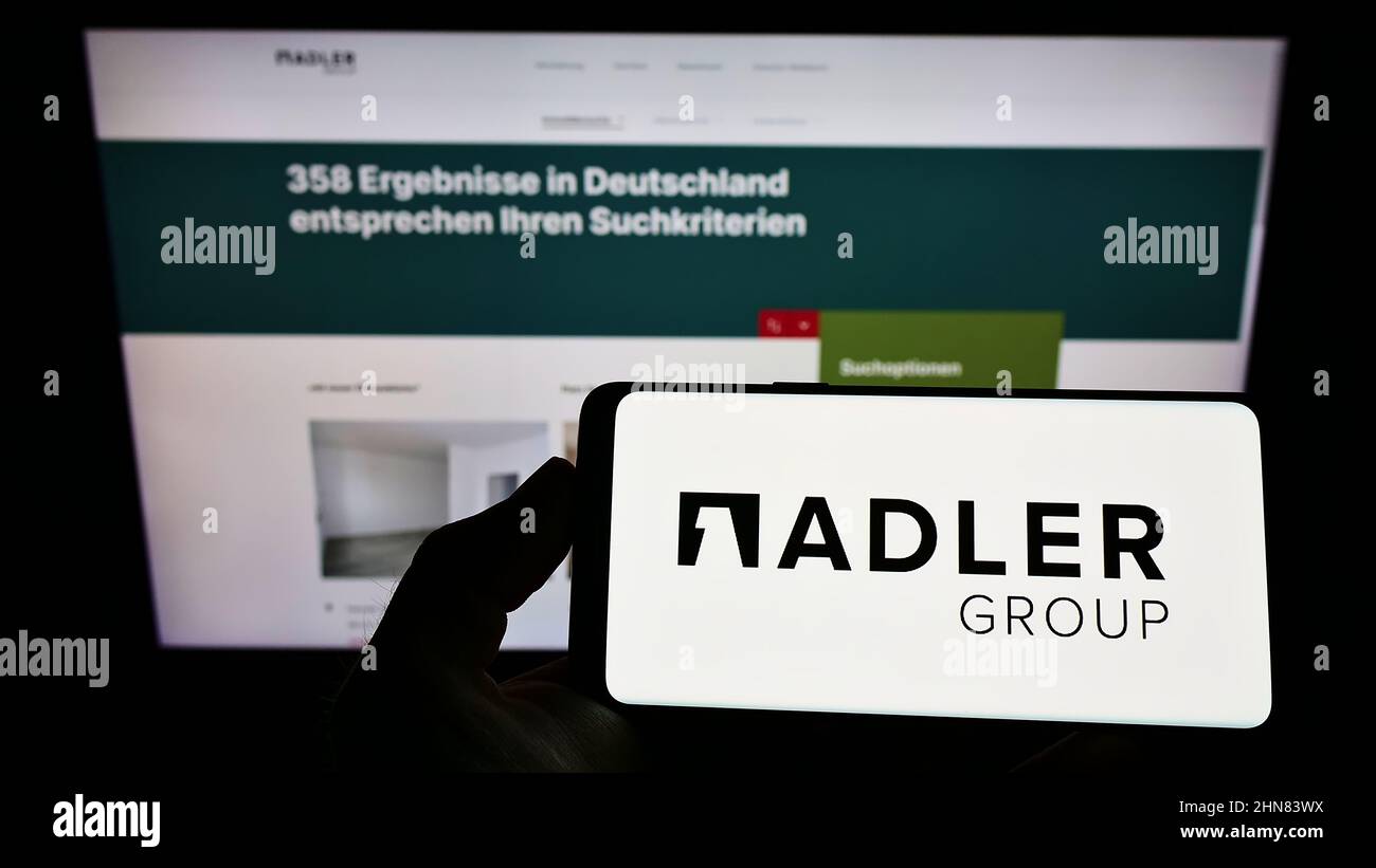 Personne tenant un smartphone avec le logo de la société immobilière Adler Group S.A. à l'écran devant le site. Mise au point sur l'affichage du téléphone. Banque D'Images