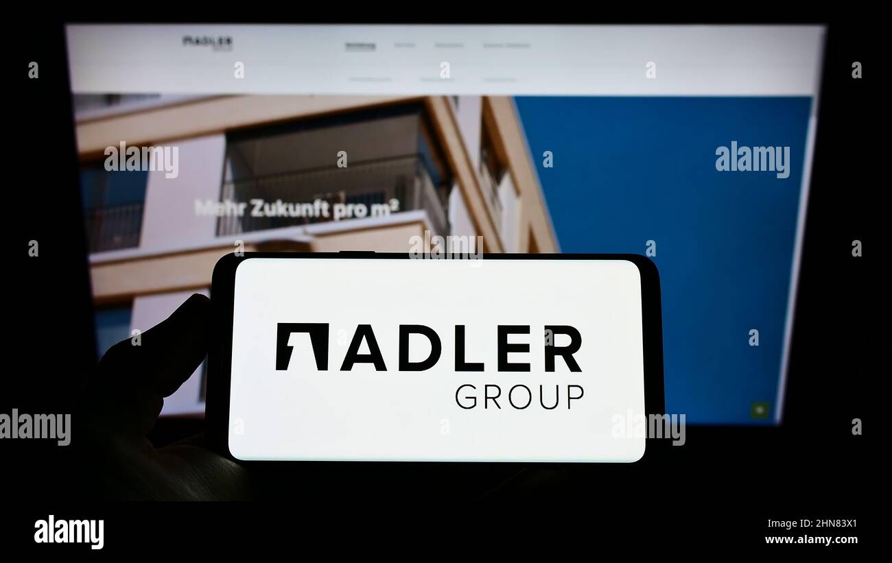 Personne tenant un téléphone portable avec le logo de la société immobilière Adler Group sa à l'écran en face de la page Web d'affaires. Mise au point sur l'affichage du téléphone. Banque D'Images