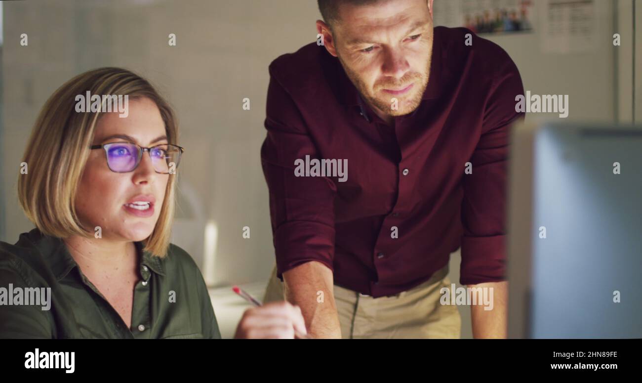 Cette équipe s'est engagée à la faire grande. 4k vidéo de deux collègues travaillant tard sur un ordinateur dans un bureau. Banque D'Images