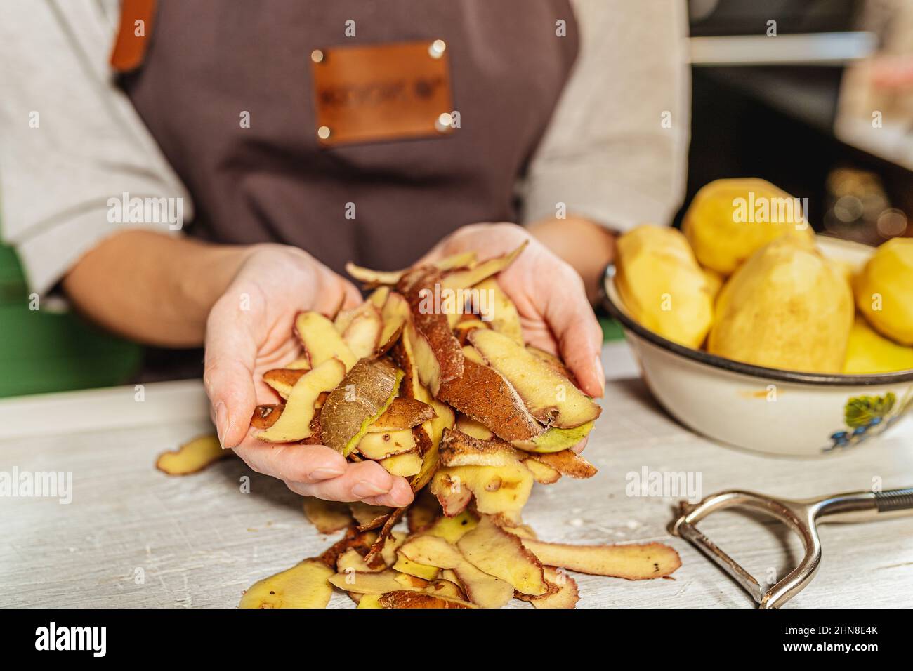 Pelures de pommes de terre dans les mains de la cuisinière femelle. Utilisation et transformation des déchets alimentaires, compostage, afin d'enrichir la fertilité des sols. Tri des ordures à la maison Banque D'Images