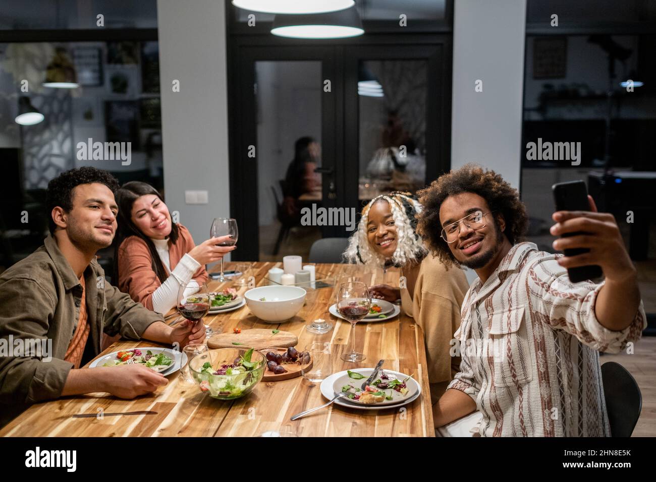 Un jeune Africain fait le portrait du selfie sur son téléphone portable avec ses amis lorsqu'ils sont assis à la table de salle à manger pendant la fête à la maison dans la cuisine Banque D'Images