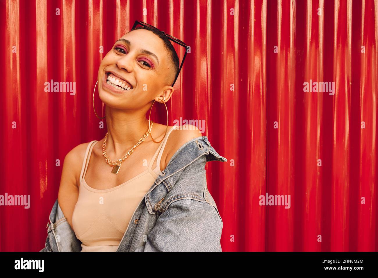 Une jeune femme heureuse souriant à la caméra tout en se tenant seule sur un fond rouge. Une jeune femme insouciante se sente vibrante et pleine de vie. Banque D'Images