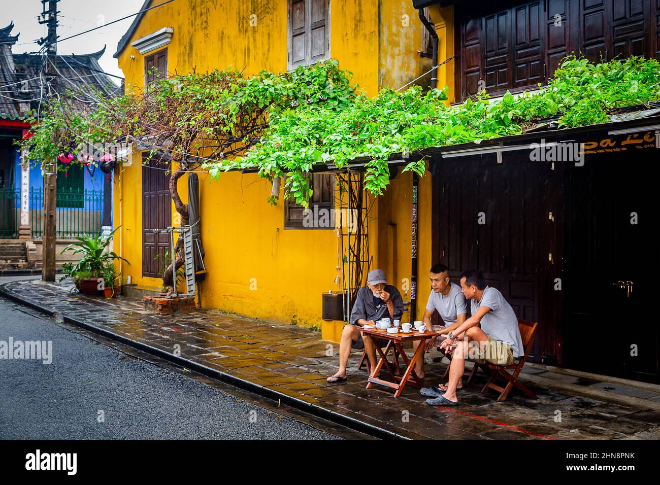 Trois hommes s'assoient sous un surplomb avec des plantes vertes pendant qu'ils pleuvent dans la vieille ville. Banque D'Images