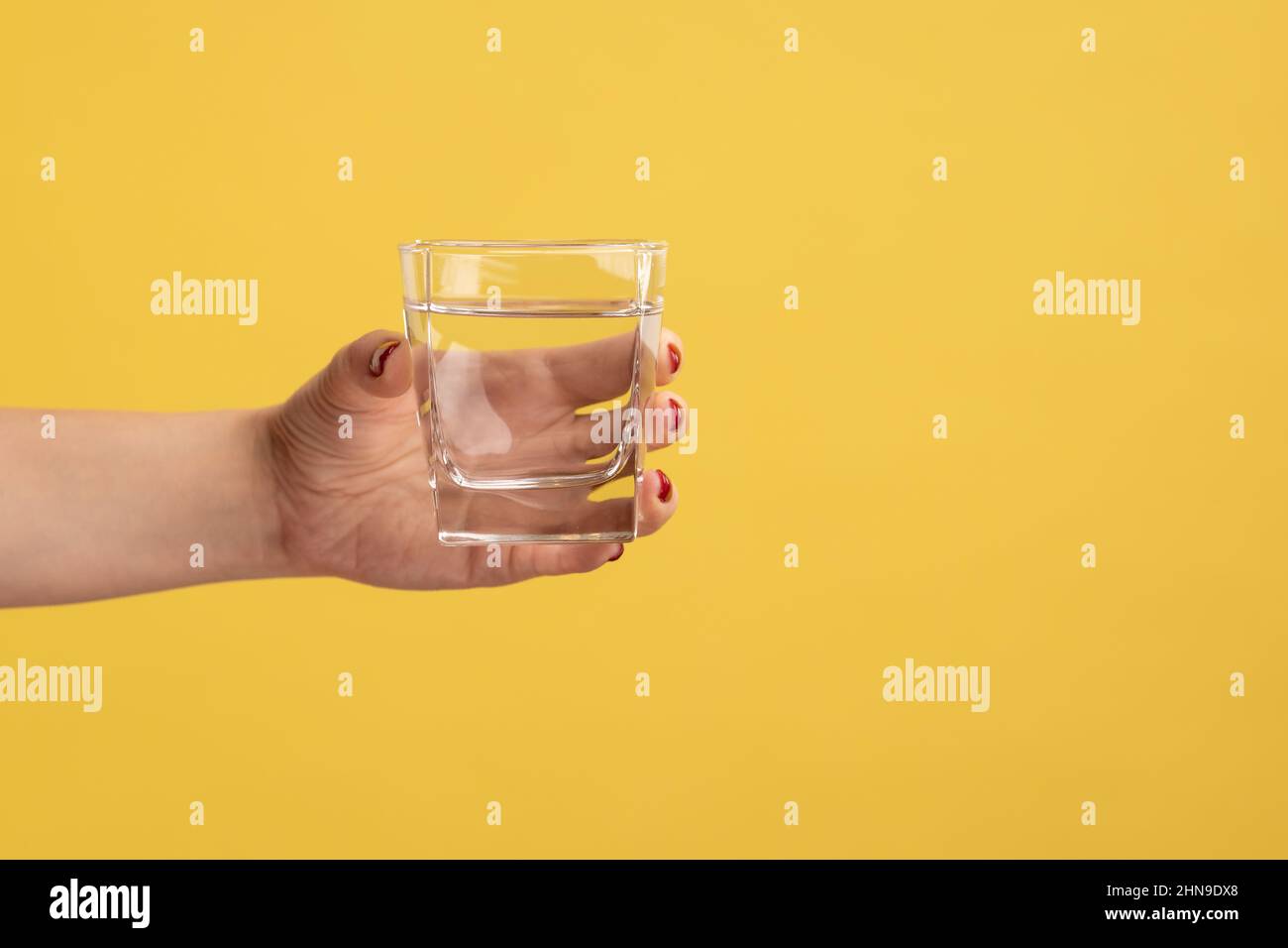 Gros plan femme main tenant le verre avec l'eau, la publicité de boisson fraîche pure, meilleur moyen de restaurer l'équilibre de l'eau. Studio d'intérieur isolé sur fond jaune. Banque D'Images
