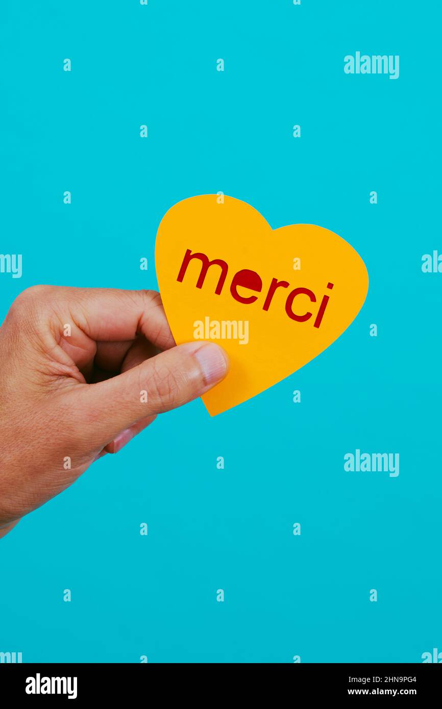 un homme caucasien a un coeur jaune dans sa main avec le texte merci écrit en français, sur fond bleu Banque D'Images