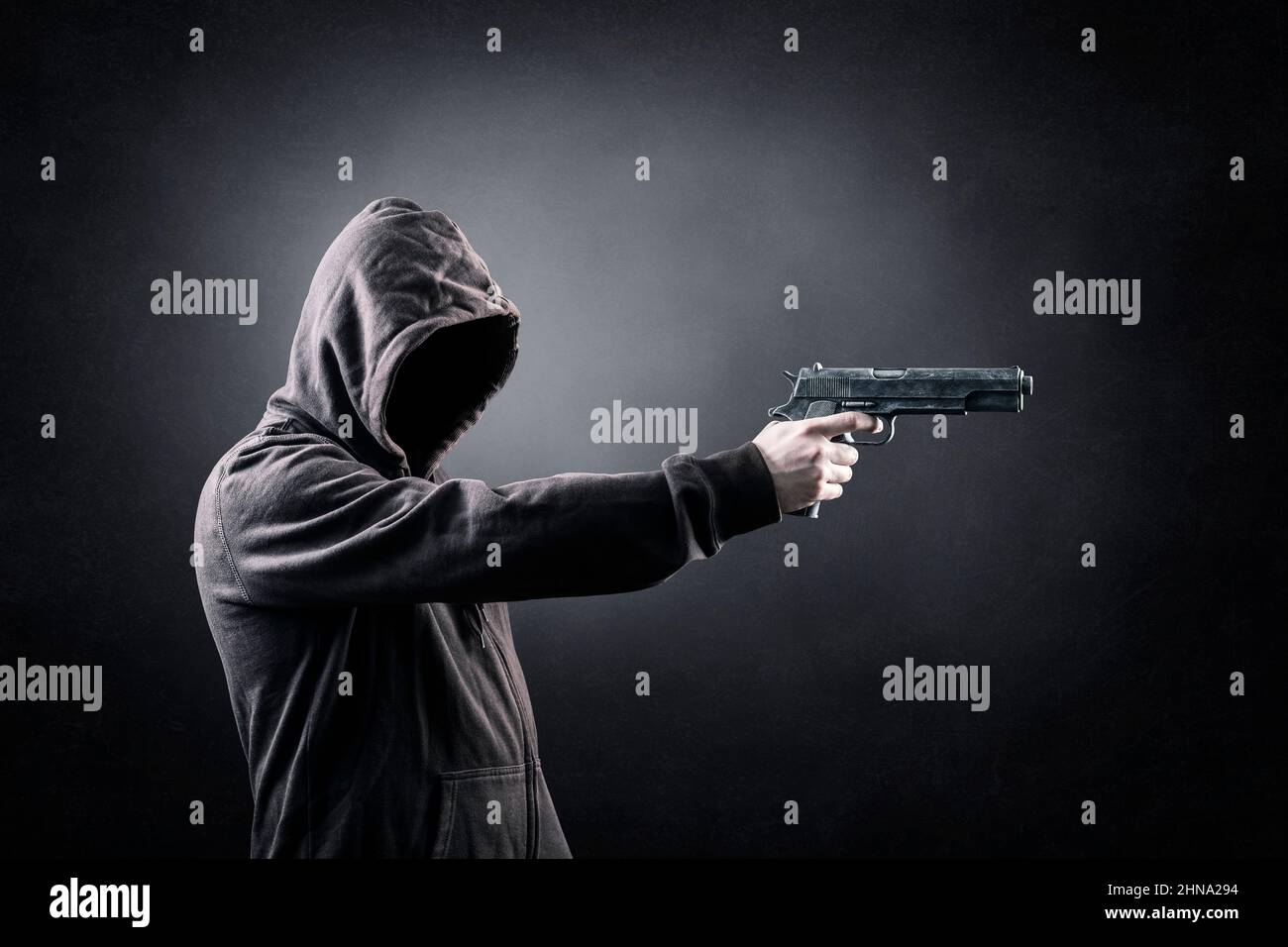 Homme cagoulé avec une arme à feu dans l'obscurité Banque D'Images