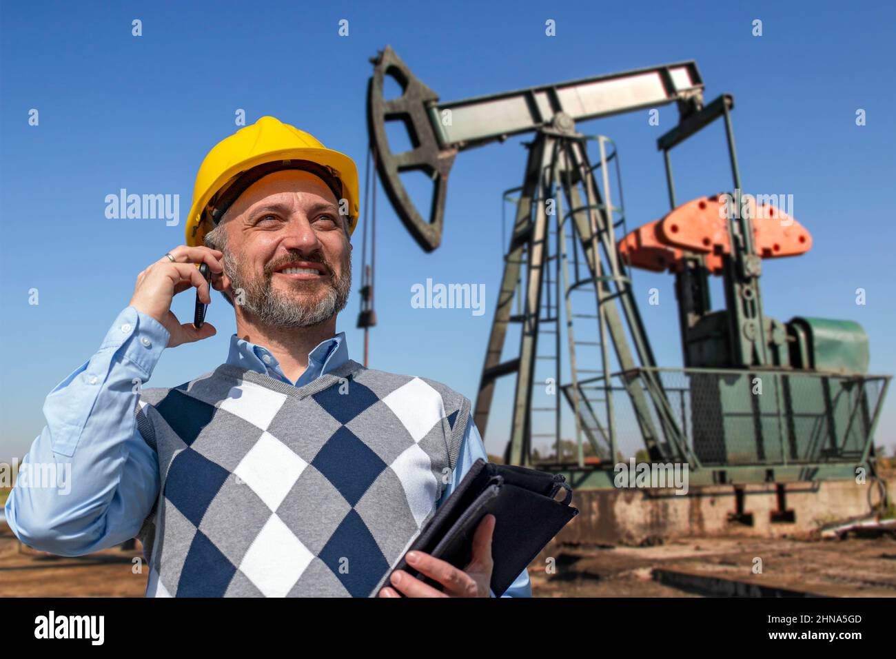 Souriant Manager ou ingénieur pétrolier de Yellow HardHat parlant sur téléphone mobile. Extraction de pétrole brut. Banque D'Images