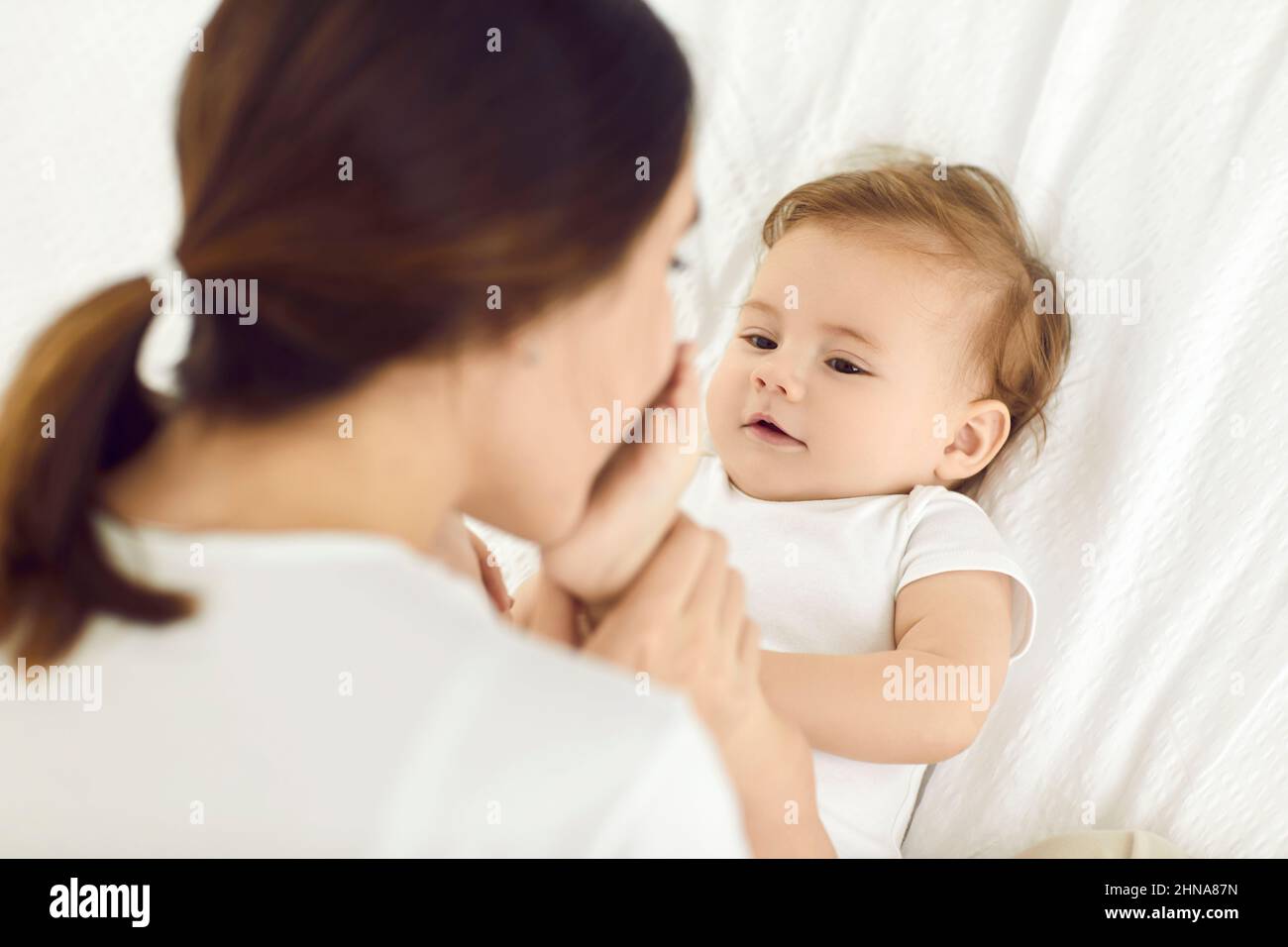 Une mère heureuse et aimante embrasse les petits pieds de son bébé garçon tout en se coulant sur le lit à la maison Banque D'Images
