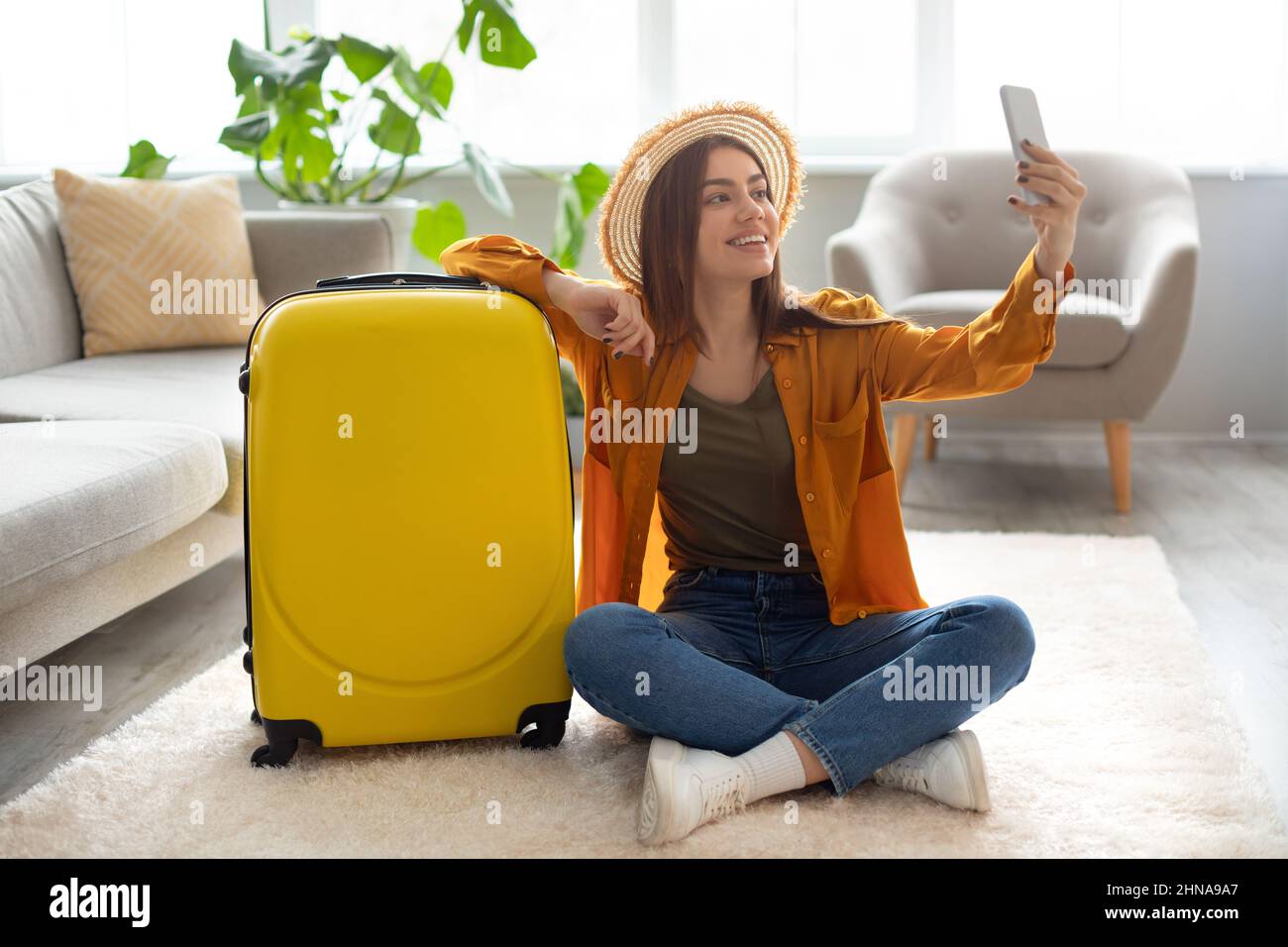 Jeune femme joyeuse avec une valise lumineuse prenant le selfie, se préparer pour les vacances à la maison Banque D'Images