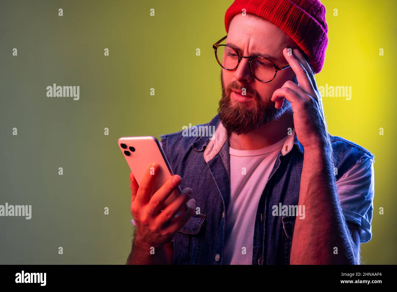 Homme hippster à la main, pensant à la mise à jour de logiciels, pensant à choisir des tarifs adaptés. Studio d'intérieur isolé sur fond de néon coloré. Banque D'Images