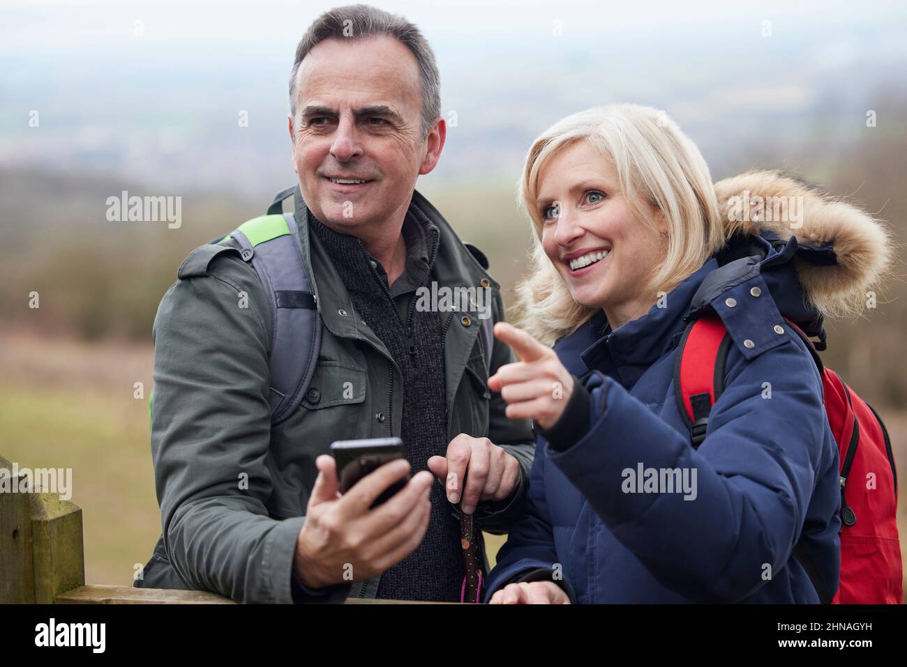 Les couples retraités d'âge mûr marchent dans la campagne d'automne ou d'hiver en utilisant la carte ou l'application de navigation sur le téléphone mobile Banque D'Images