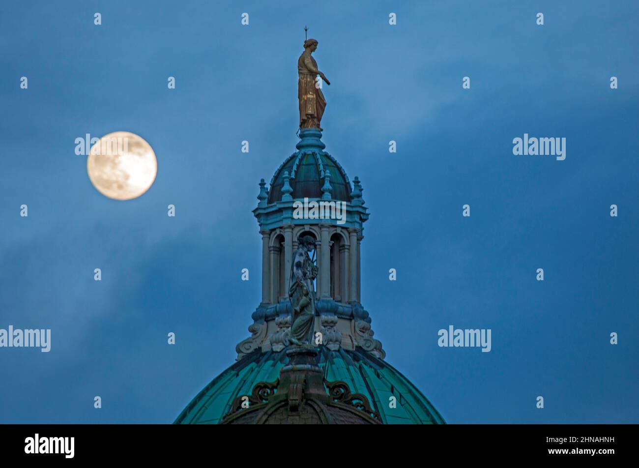 Édimbourg, Écosse, Royaume-Uni. 15th février 2022. Snow Moon Rising qui sera un 100% complet demain, apparaissant dans le ciel derrière la statue représentant la renommée au-dessus du dôme octogonal central de l'ancien siège de la Banque d'Écosse sur le Mound. Temps très nuageux avec des écarts occasionnels dans le nuage et la température de 4 degrés centigrade et de fortes pluies juste après cette prise de vue. Banque D'Images