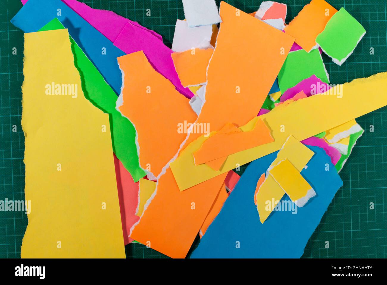 Morceaux de papier déchirés de couleur néon sur fond vert foncé. Banque D'Images