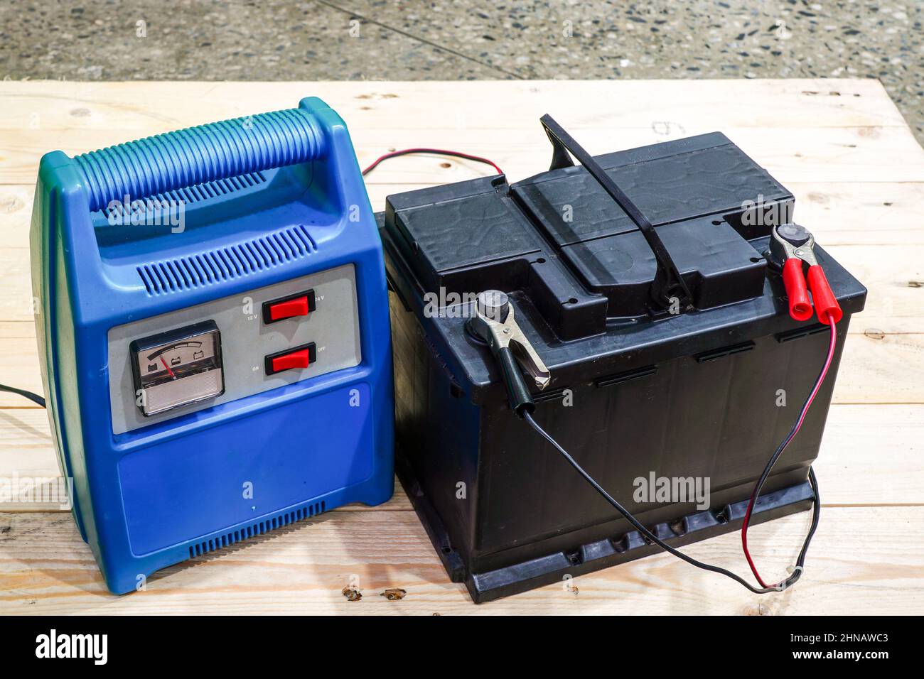 chargeur de batterie bleu câblé à une batterie de voiture noire sur une  palette en bois, la charge est en cours Photo Stock - Alamy