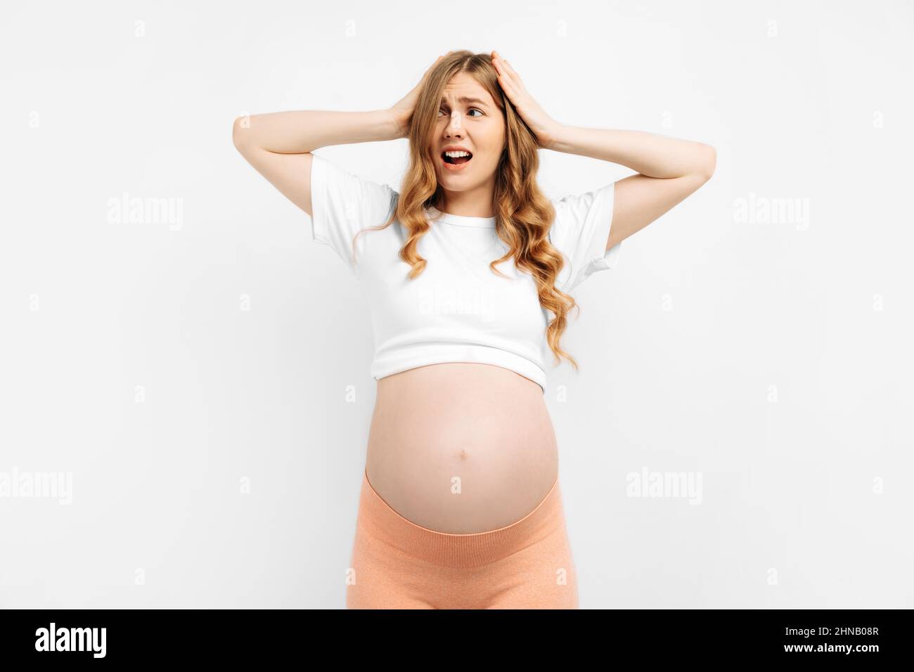 J'ai peur. Portrait d'une femme enceinte effrayée et incertaine se tenant isolée sur fond blanc de studio. Femme nerveuse excitée expériences avant la grossesse Banque D'Images