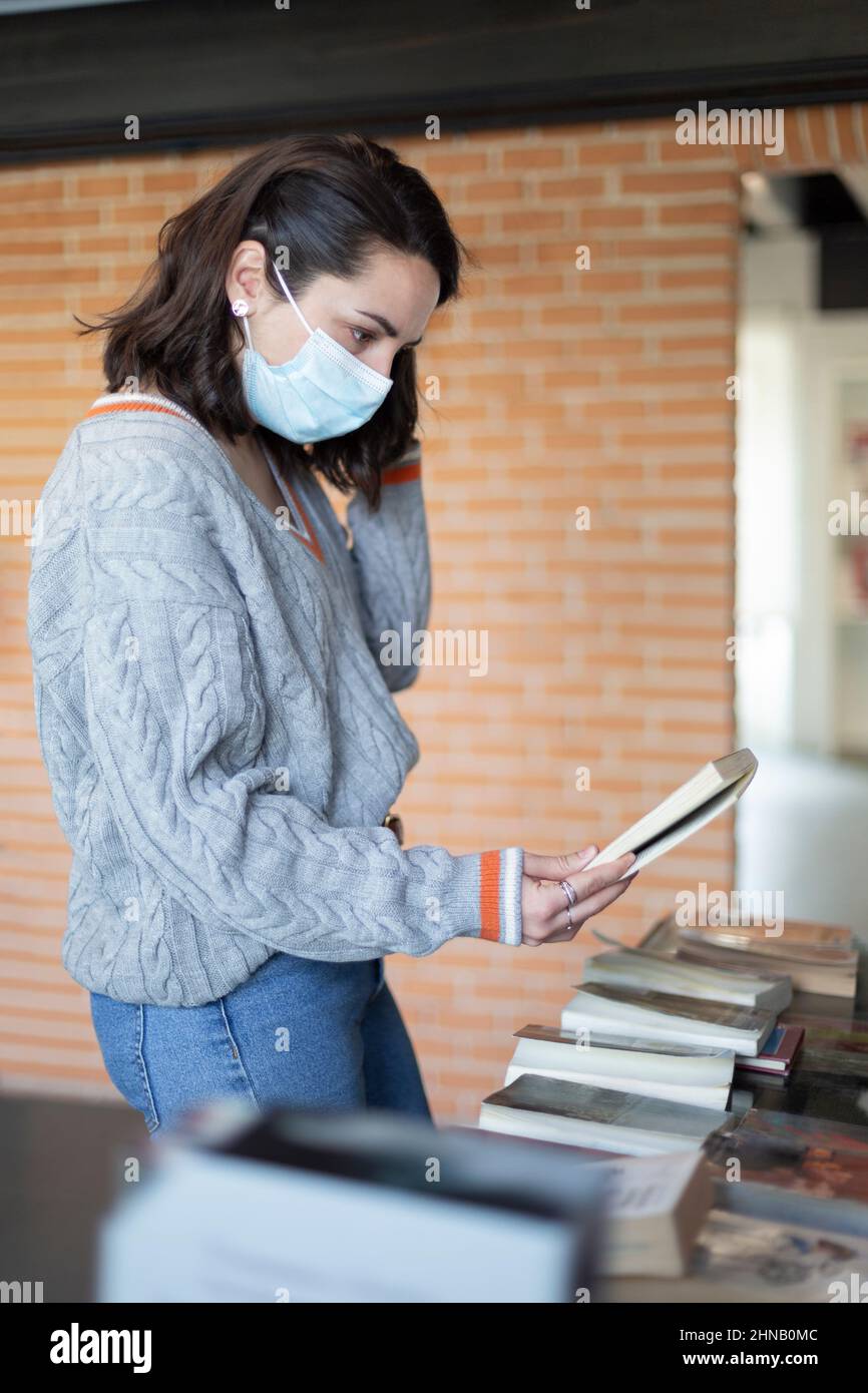 Jeune femme avec masque de visage choisir des livres dans une librairie. Banque D'Images