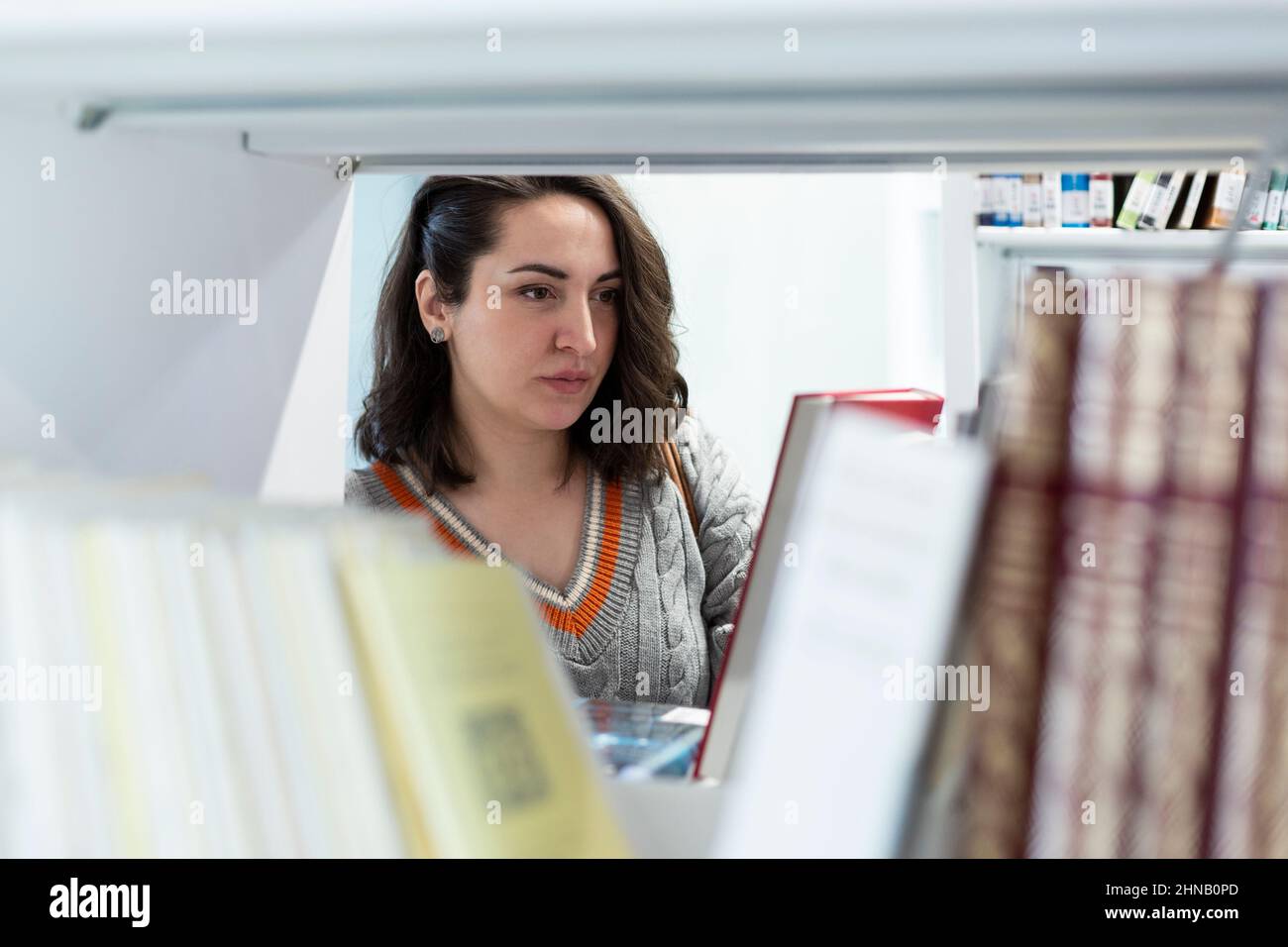 Jeune femme caucasienne regardant des livres dans une bibliothèque. Mise au point sélective. Espace pour le texte. Banque D'Images