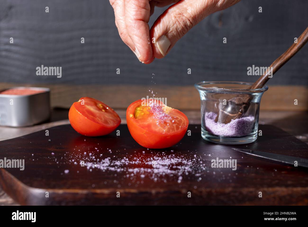 Chef salant une tomate en deux sur une planche à découper en bois Banque D'Images