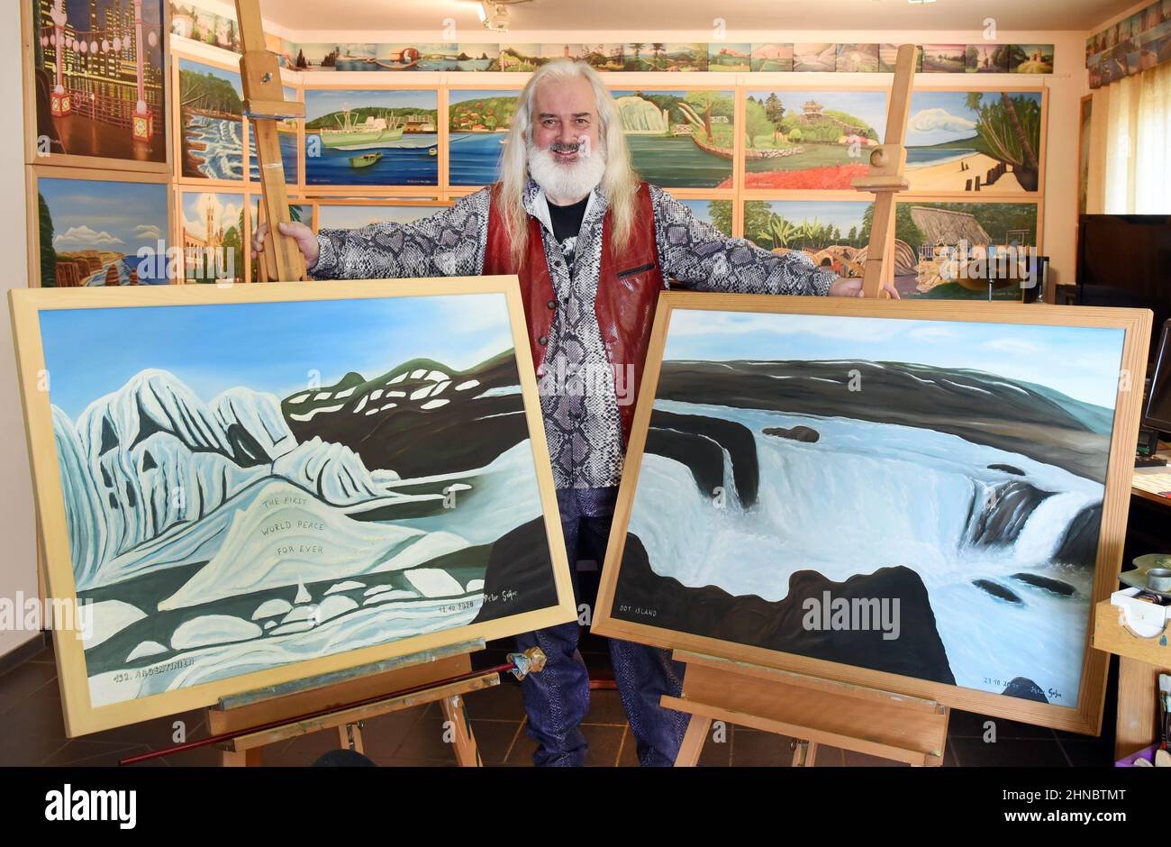 14 février 2022, Saxe-Anhalt, Spergau, BEI Leuna: L'artiste Peter Gehre se trouve dans son salon, qu'il utilise également comme studio, salle de musique et bureau, entouré de photos de sa peinture, qui à 192 mètres est la plus longue au monde. L'homme de 65 ans cherche d'urgence un lieu d'exposition, ou comme il le dit, un millionnaire, pour sa "Vision de l'Union mondiale", qui se compose de 192 peintures à l'huile. Le lien et la transition sans heurt d'une peinture, et donc d'un pays à l'autre, est la vision de l'homme de 65 ans de l'égalité des droits pour tous les pays et d'un monde pacifiquement uni. Banque D'Images