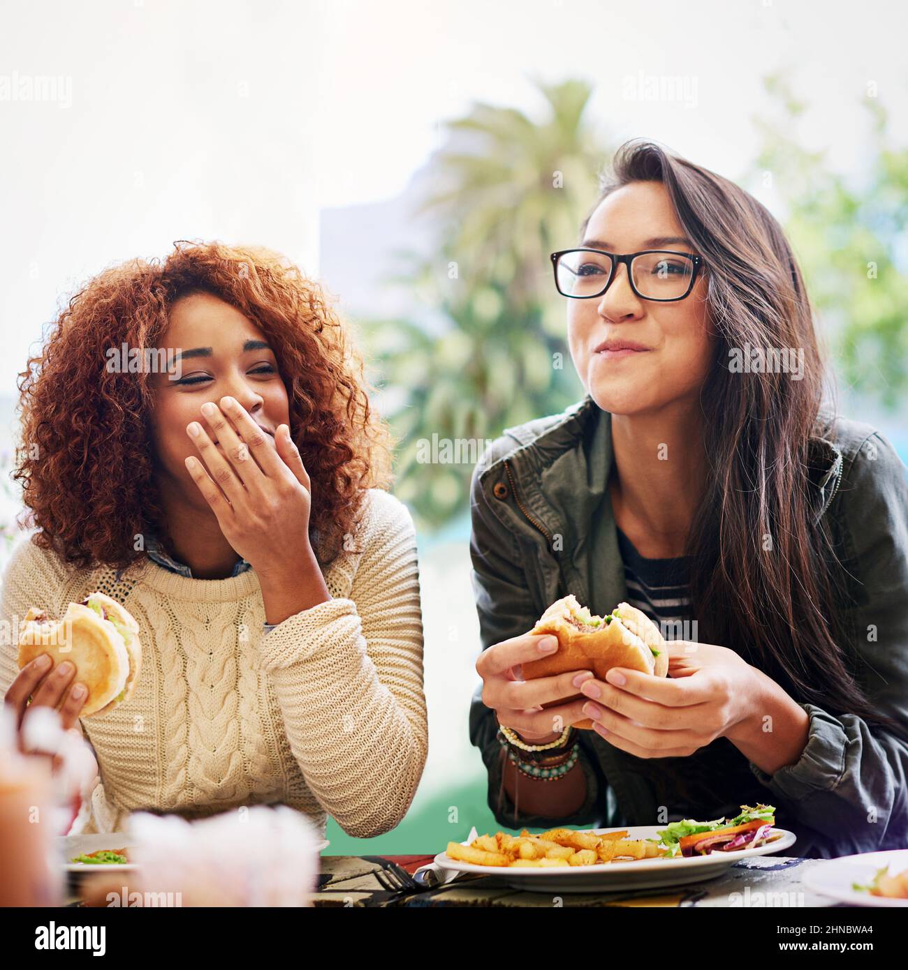Partager de la bonne nourriture et de bonnes blagues. Photo de deux petites amies mangeant des hamburgers à l'extérieur. Banque D'Images
