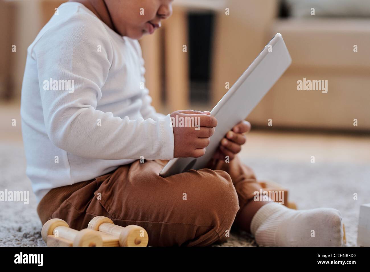 Gros plan d'un tout-petit noir assis avec des jambes croisées sur le tapis et à l'aide de l'application d'apprentissage sur la tablette Banque D'Images