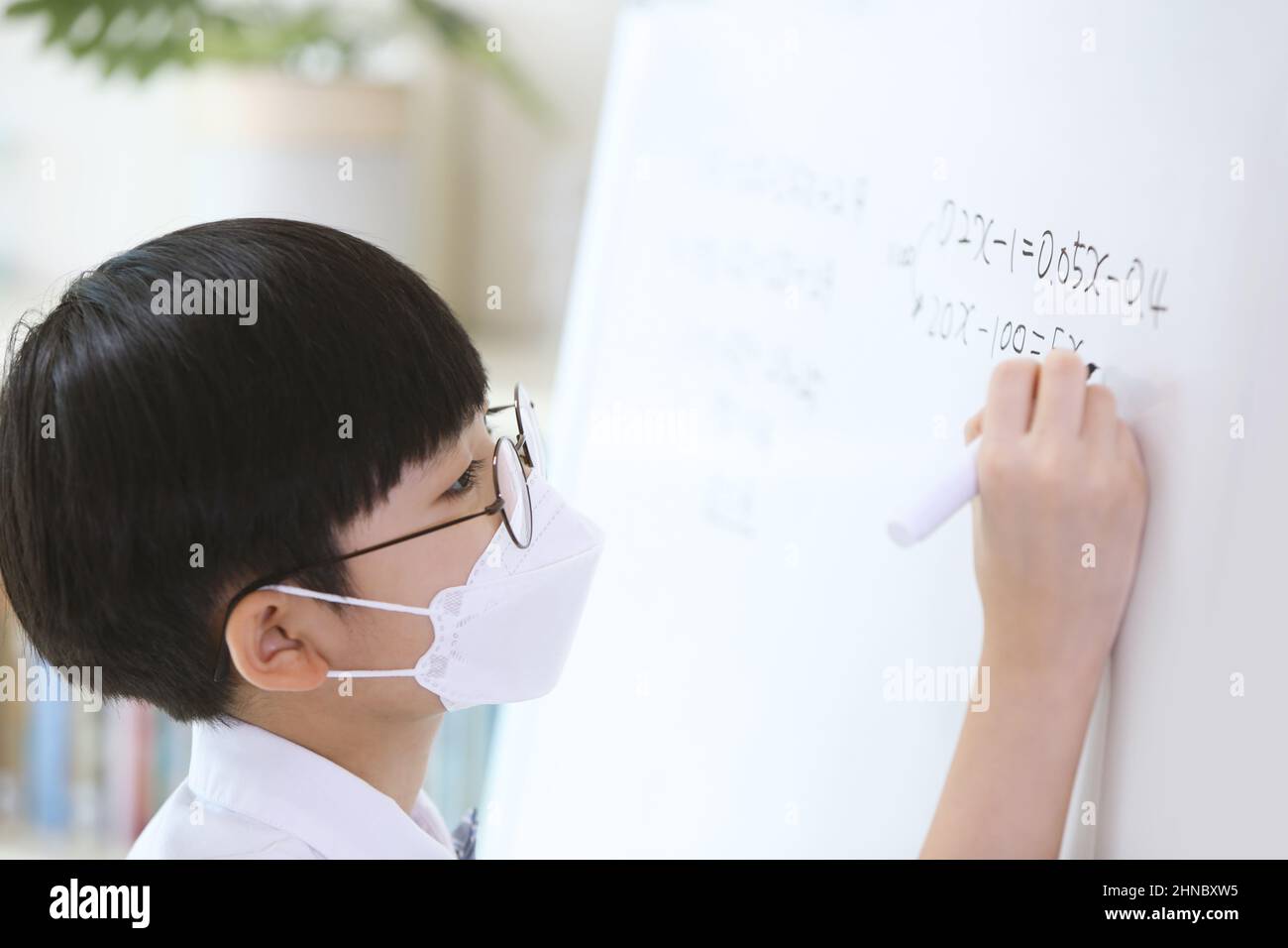 Un garçon élégant et mignon qui se concentre sur ses études tout en travaillant dur sur le tableau noir pour résoudre des problèmes mathématiques Banque D'Images