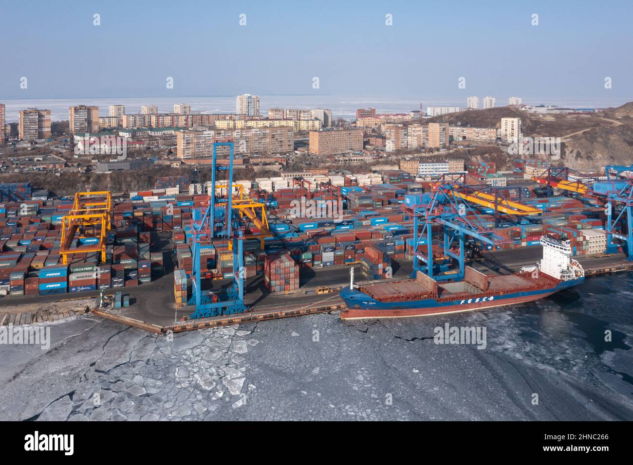 Vladivostok, Russie - 27 janvier 2022 : Vue de dessus du terminal des conteneurs du port maritime et de la ville.En hiver, un bateau à conteneurs est en train de charger au quai. Banque D'Images
