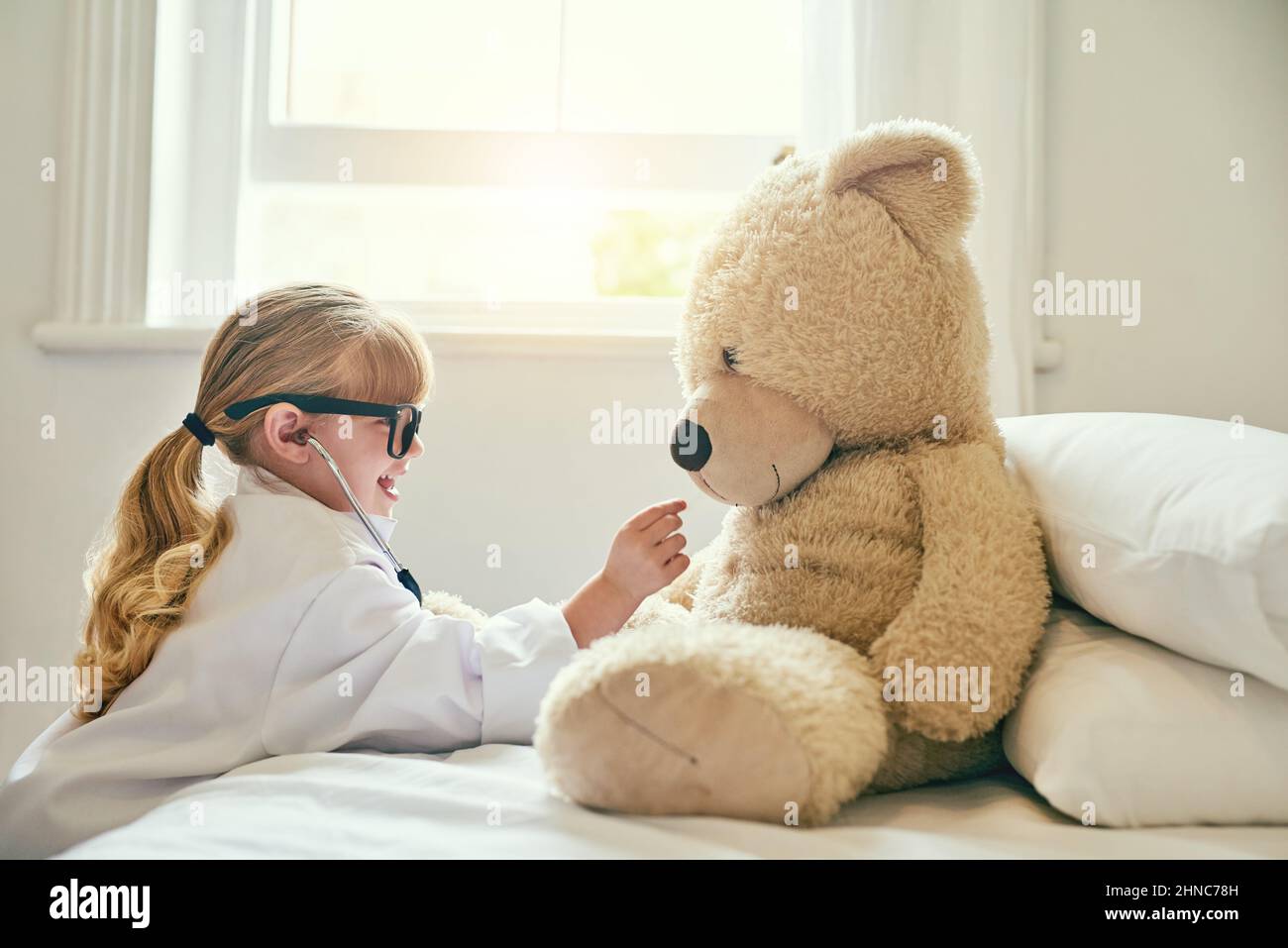 C'est un bon coeur que vous avez là, teddy. Photo d'une adorable petite fille vêtue comme médecin et examinant un ours en peluche avec un stéthoscope. Banque D'Images