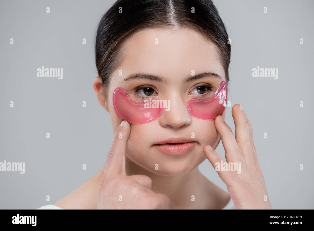 Jeune femme avec le syndrome de Down appliquant des taches oculaires isolées sur le gris Banque D'Images