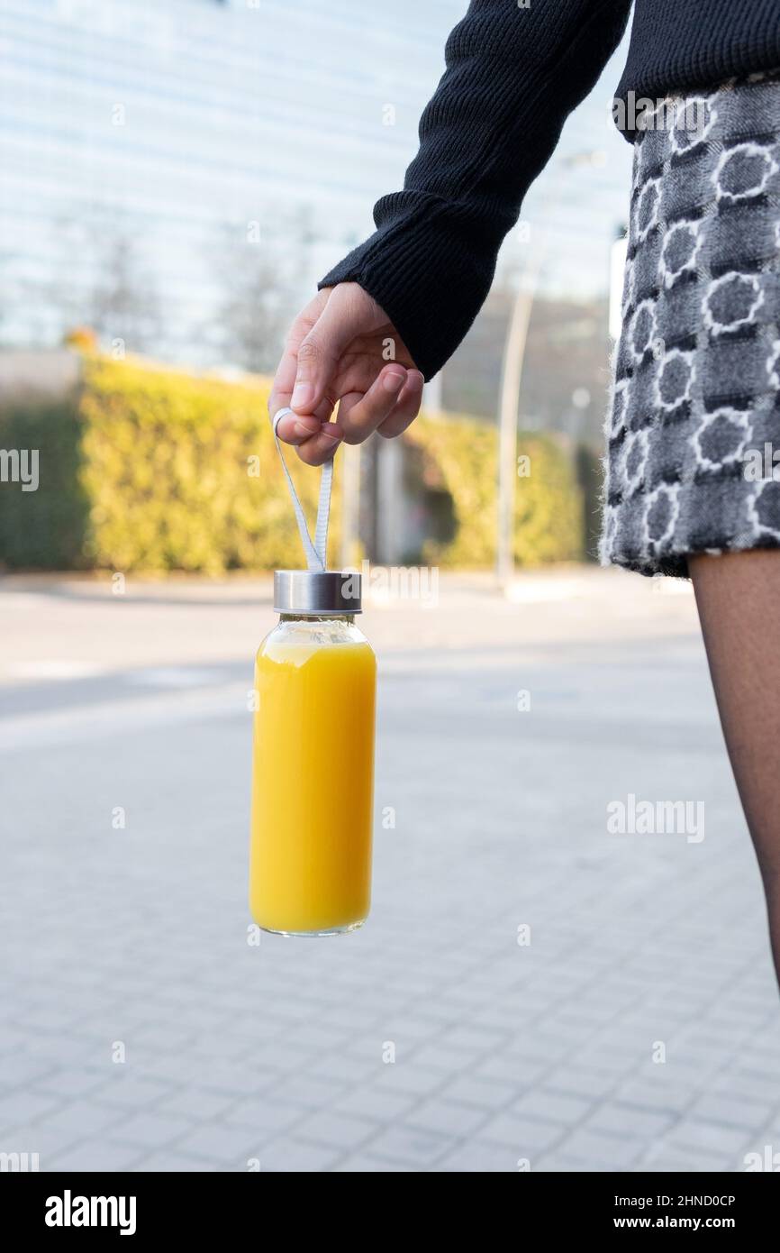 Crop anonyme femelle en jupe avec bouteille de verre de jus d'orange frais  à la main debout sur la rue pavée dans la ville Photo Stock - Alamy