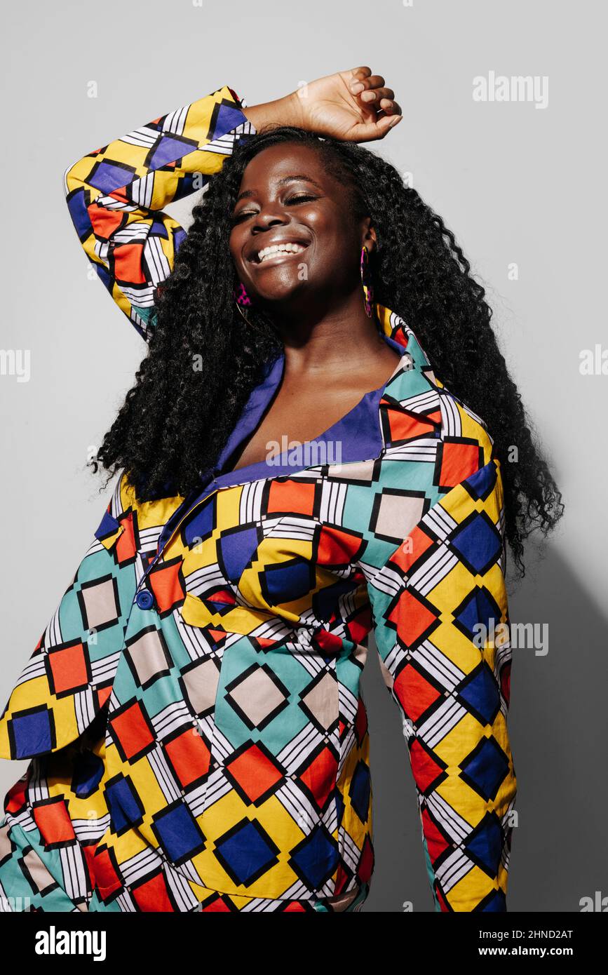 Bonne femme afro-américaine aux cheveux bouclés dans une tenue élégante en souriant sur fond blanc avec main sur la tête Banque D'Images