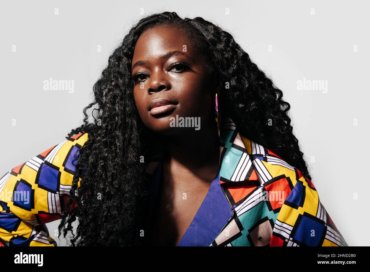 Jeune femme afro-américaine sérieuse avec des cheveux bouclés et des vêtements colorés lumineux sur fond blanc Banque D'Images