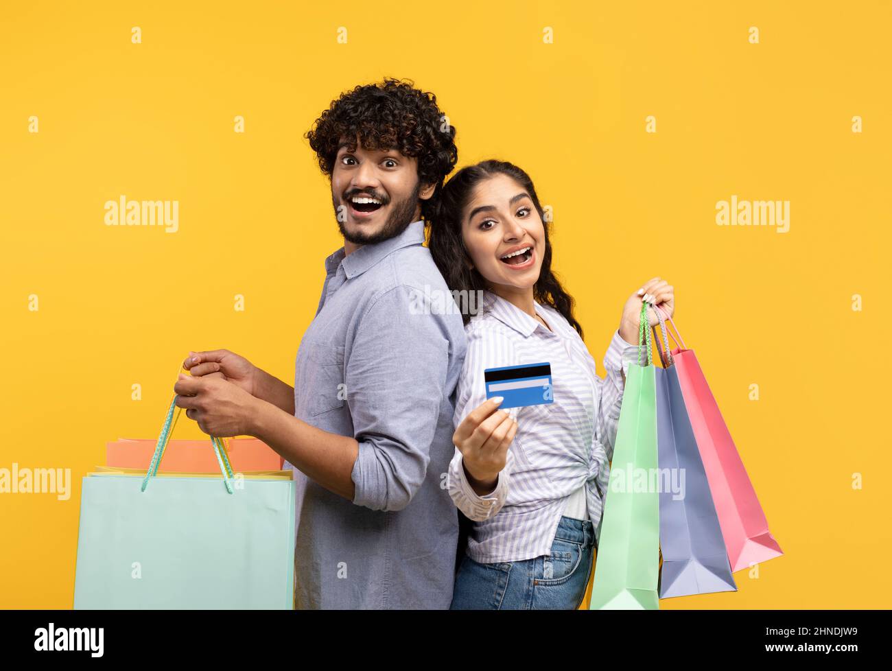 Portrait d'une famille indienne excitée tenant des sacs de shopping et une carte de crédit sur fond jaune de studio Banque D'Images