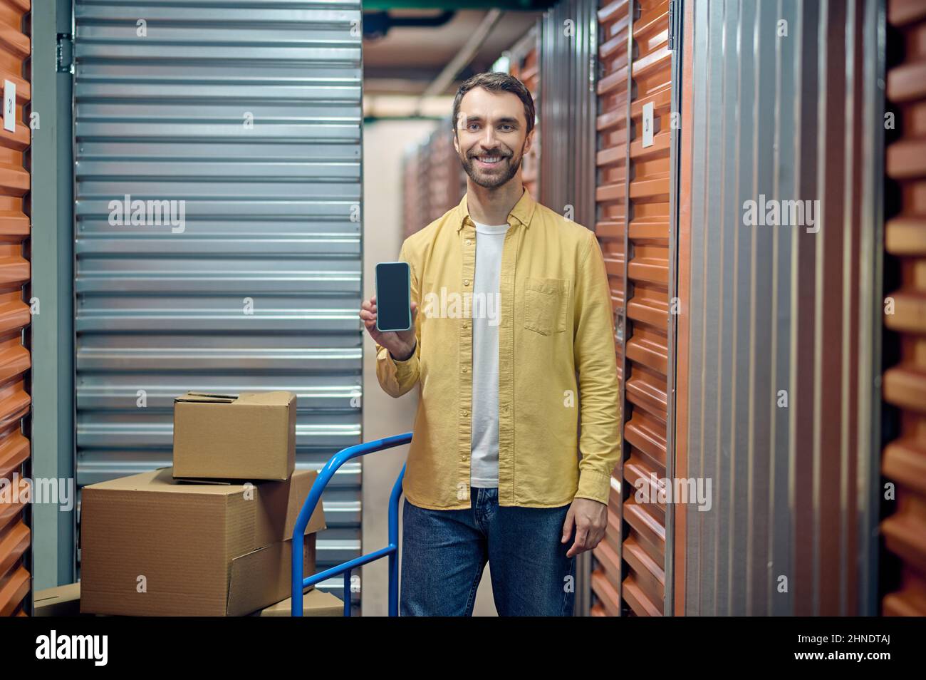 Joyeux préparateur de commande masculin montrant son téléphone portable Banque D'Images