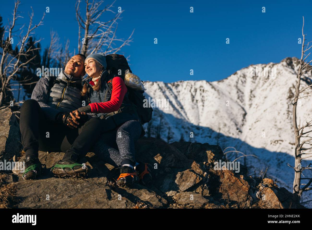 Homme et femme en vêtements de sport s'assoient sur la colline. Couple de voyageurs charmants à tenir, appréciant le paysage des hautes terres, beau coucher de soleil. Deux touristes font de la randonnée sur fond de montagnes enneigées. Banque D'Images