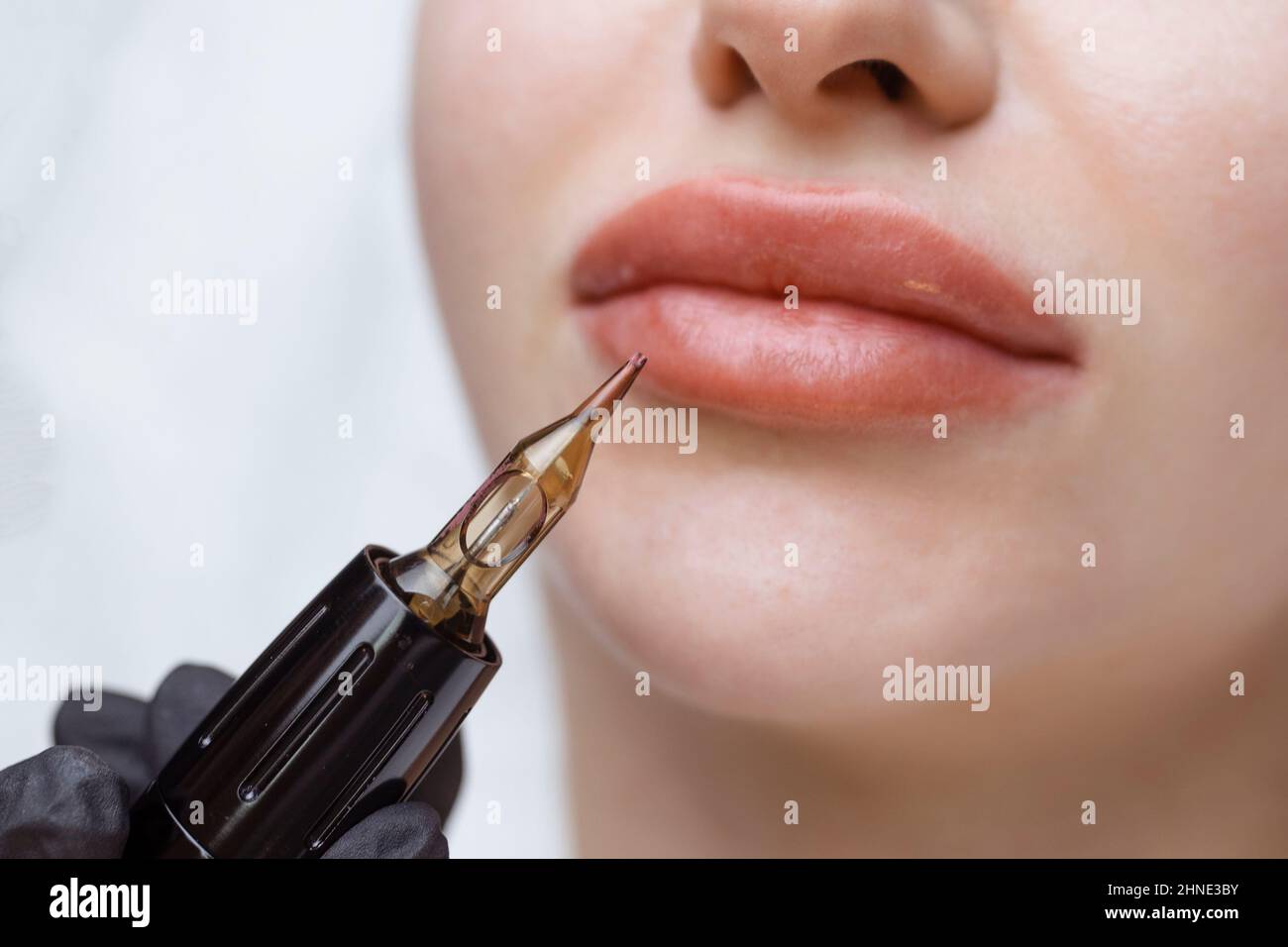 Le cosmétologue fait un maquillage permanent sur le visage d'une femme. Un spécialiste applique un tatouage sur les lèvres du patient en gros plan Banque D'Images