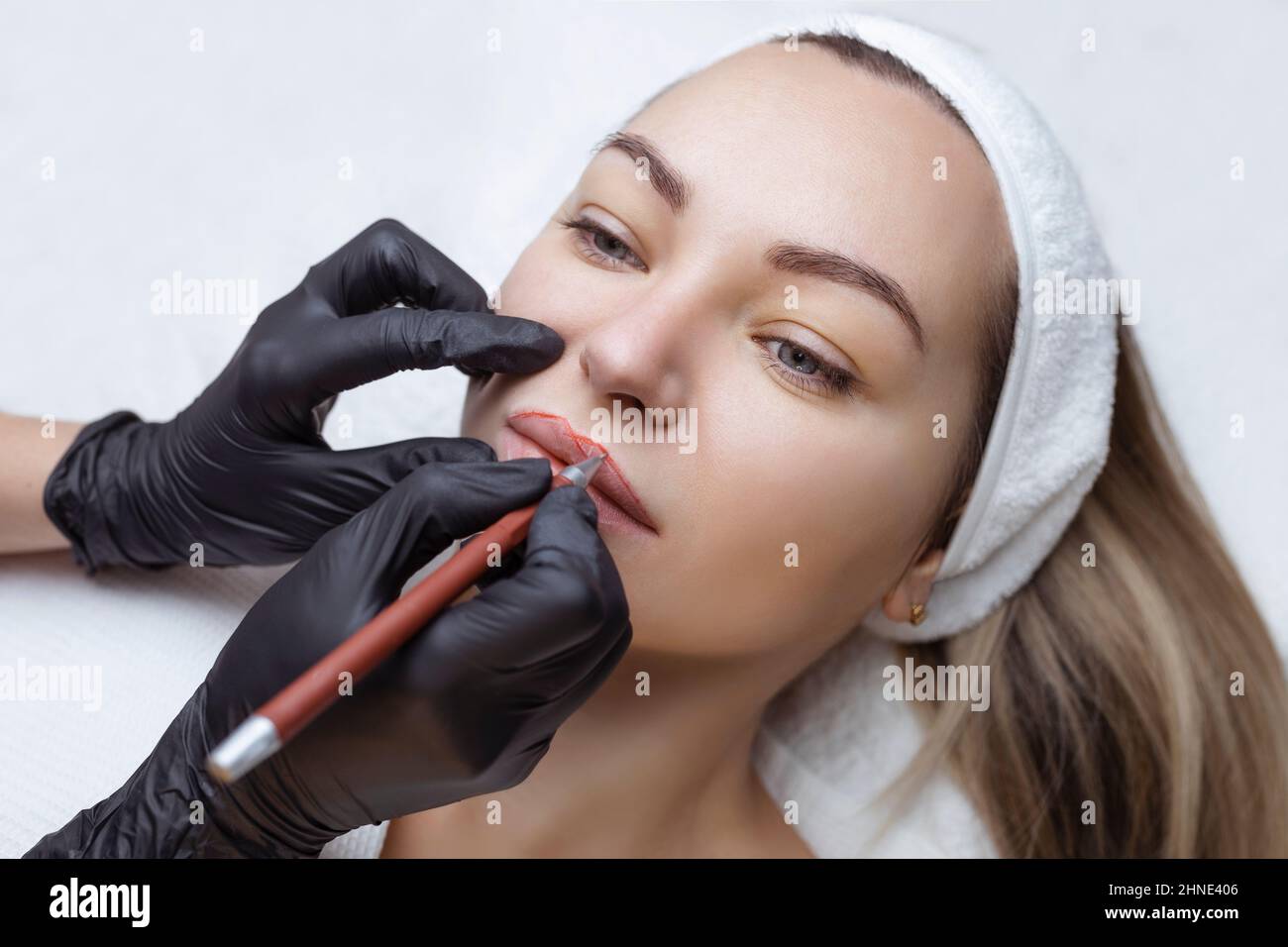 Jeune femme avec maquillage permanent sur ses lèvres dans un salon de cosmétologues. Tatouage de maquillage permanent. Dessinez une ligne avec un crayon rouge à lèvres Banque D'Images