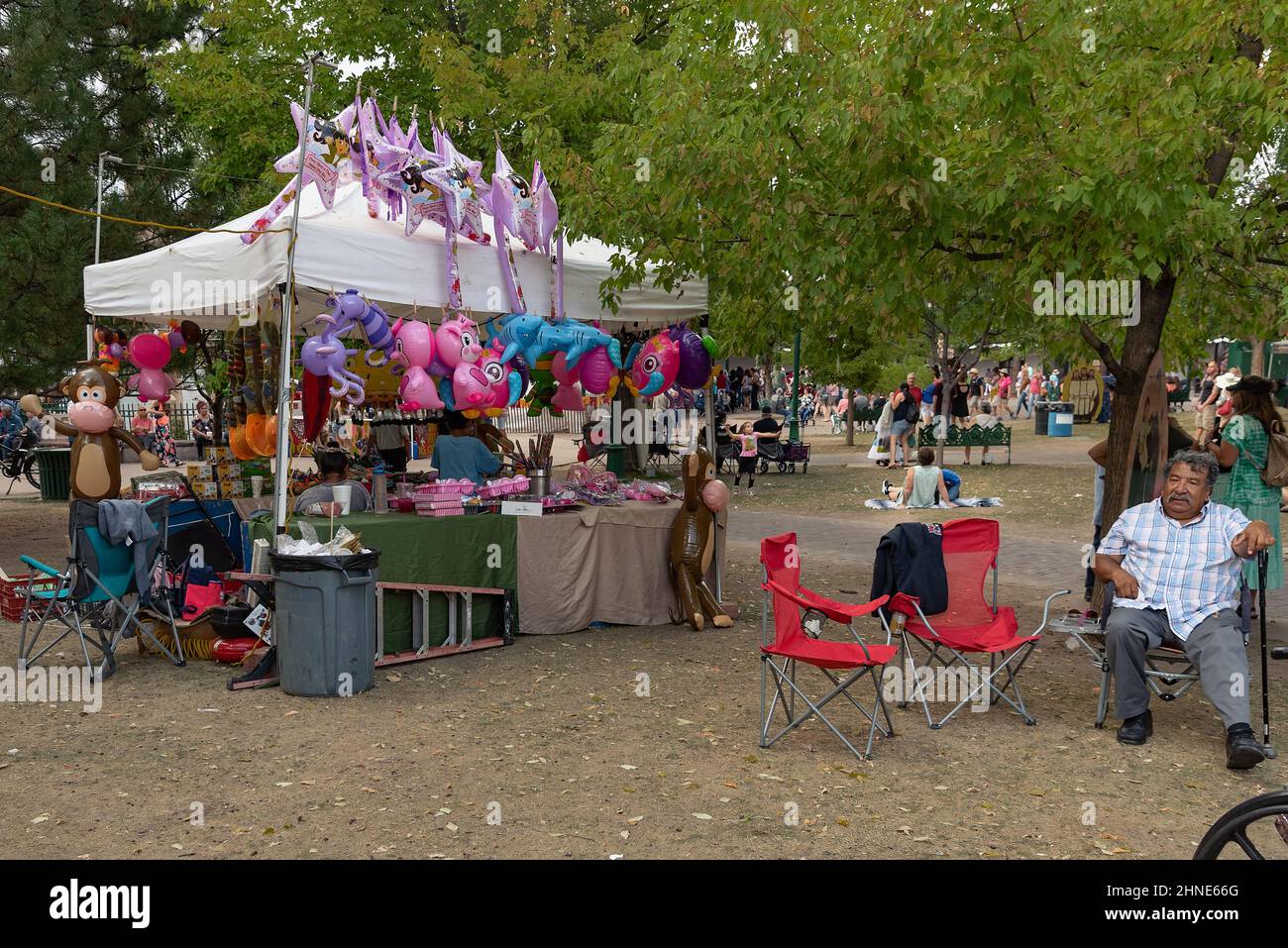 Un homme est assis dans une chaise pliante près d'un stand de vendeur qui vend des jouets gonflables dans la place Santa Fe pendant la Fiesta de Santa Fe 307th au Nouveau-Mexique. Banque D'Images