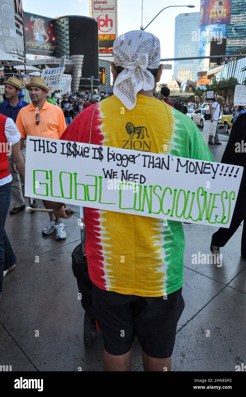 Un homme portant un foulard sur sa tête et une chemise rouge, jaune et verte descend Las Vegas Boulevard avec un signe de protestation sur son dos. Banque D'Images