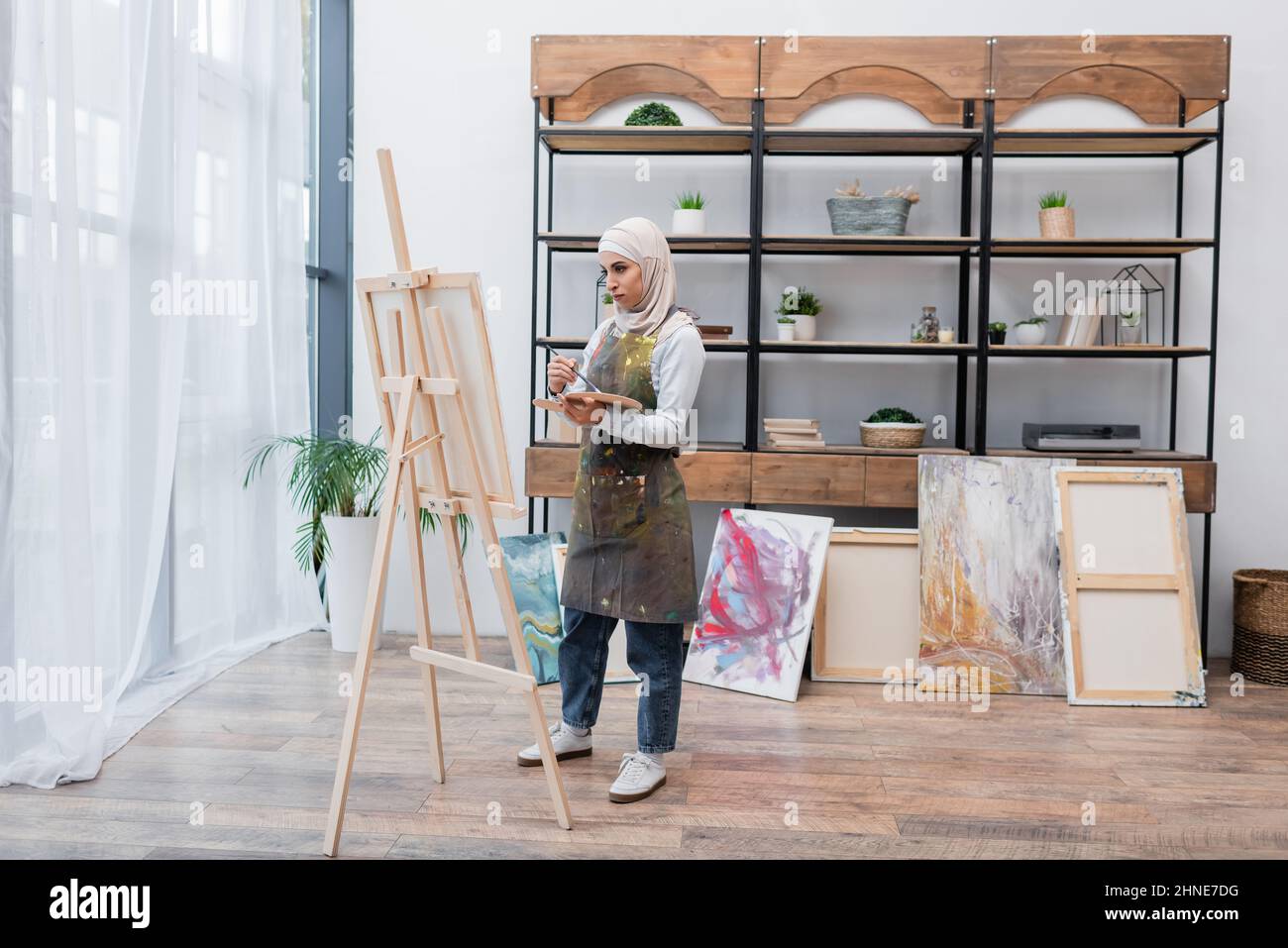 vue en longueur de la femme musulmane qui dessine sur un chevalet près des photos peintes dans le studio à la maison Banque D'Images